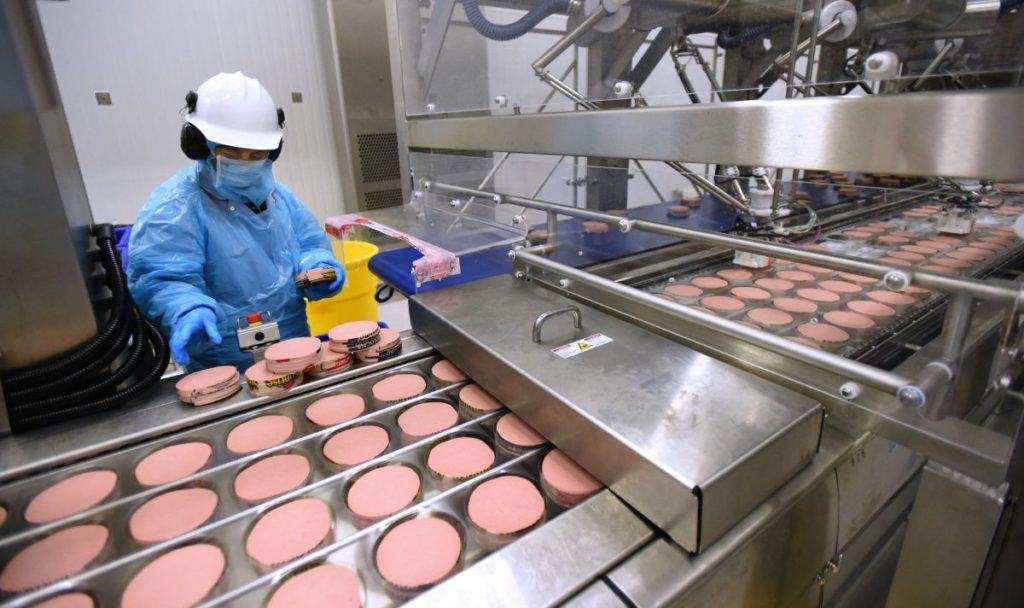 Frontline food worker wearing an N95 mask and inspecting processed meat